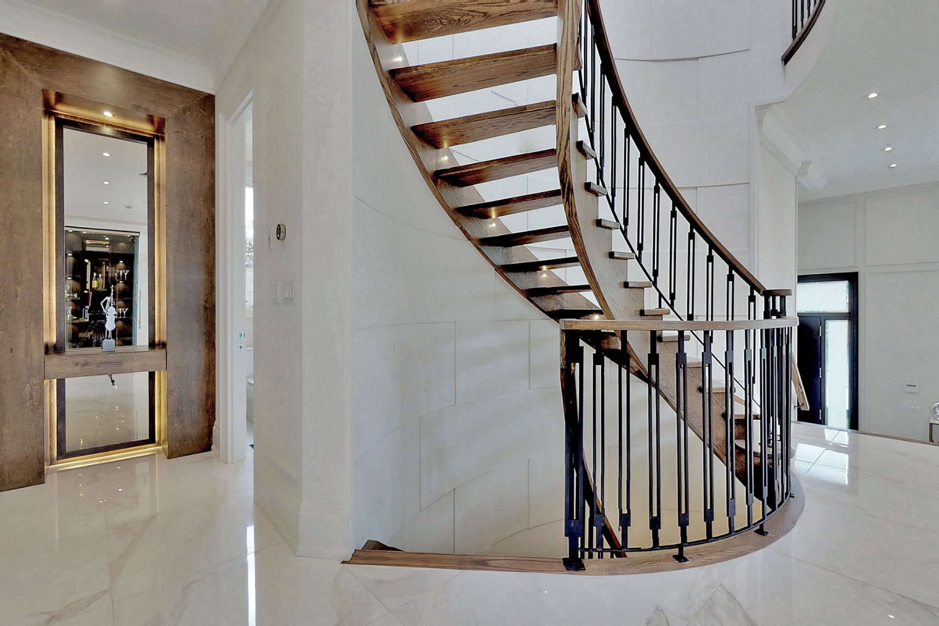 Curved floating staircase with dark wood treads, black metal balusters and integrated riser lighting
